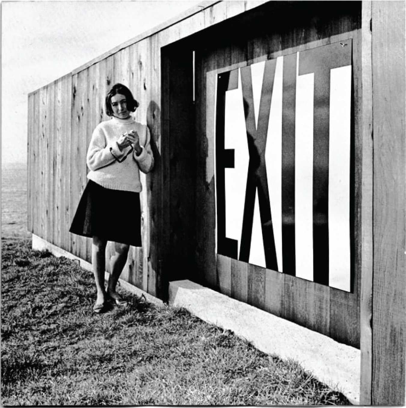 Barbara Stauffacher Solomon with “Exit” sign mock-up at Demonstration House, The Sea Ranch, California,